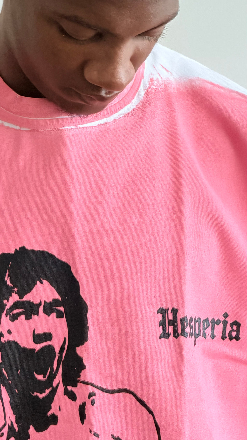 A close-up of a person wearing a pink t-shirt with a black graphic print of a screaming face and the word 'Hesperia' in a gothic font.