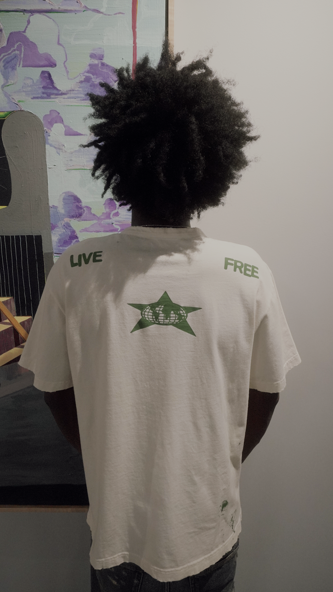 A person viewed from behind wearing a white short-sleeve T-shirt with green text reading 'LIVE' on the left shoulder, 'FREE' on the right shoulder, and a green star graphic with white text across the upper back.