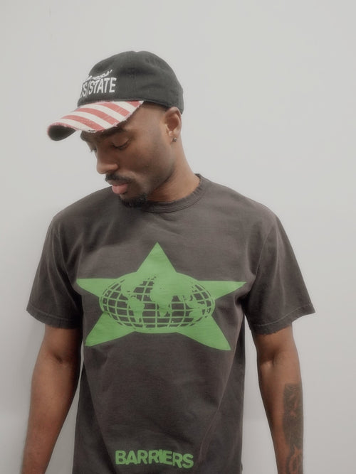 A man wearing a dark gray t-shirt with a green star and globe graphic, paired with a black and red striped baseball cap. The t-shirt features the brand name 'BARRIERS' printed near the bottom.